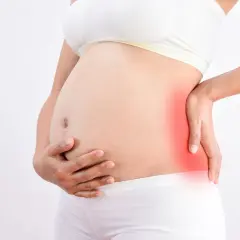 Femme enceinte tenant son ventre, une zone rouge sur le côté indique une douleur au fessier en fin de grossesse.
