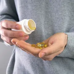 Main tenant une capsule d'huile de poisson dans sa main, prêt à prendre son complément. Avis sur les oméga 3.