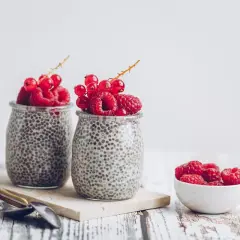 Deux pots de crème de chia garnis de framboises et de groseilles. Un petit bol de framboises à côté. Parfait pour une graine de chia enceinte.