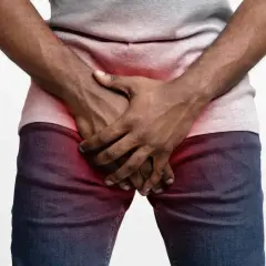 Homme tenant ses mains sur son pubis, zone rouge indiquant une douleur ou une gêne.