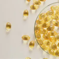 Gélules d'huile de poisson oméga 3 translucides, certaines dans une coupelle en verre, sur fond clair.