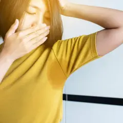 Une femme se couvre le nez, gênée par sa transpiration qui sent fort depuis peu. Une auréole de sueur est visible sous son bras.