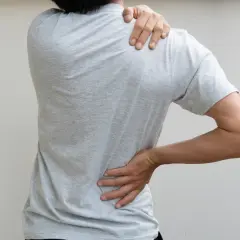 Person ressentant une douleur au haut du dos bloqué, une main sur l'épaule, l'autre sur la hanche.