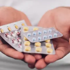 Mains tenant plusieurs plaquettes de pilules, dont des gélules rouges et blanches, des comprimés bleus et des comprimés jaunes. Que prendre avec des antibiotiques ?