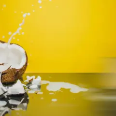 Un coco ouvert éclabousse du lait blanc sur un fond jaune vif, évoquant les nombreux lait de coco bienfaits.