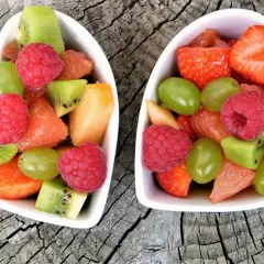Deux bols en forme de cœur remplis de fruits non acides : fraises, framboises, kiwis, raisins, melon et pamplemousse.