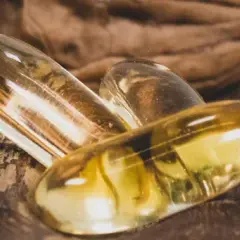 Trois capsules d'oméga 3 dorées reposent sur une noix. Quand prendre oméga 3 pour un bien-être optimal ?