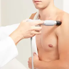 Thérapeute appliquant des ondes de choc radiales sur l'épaule d'un patient pour soulager la douleur.