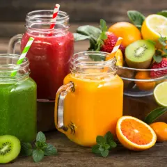 Trois smoothies colorés (vert, rouge, orange) dans des bocaux en verre, accompagnés de fruits frais. Parfait pour une cure detox maison.