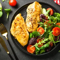 Deux blancs de poulet grillés avec une salade fraîche. Un repas sain, idéal pour savoir quels aliments éviter quand on a du cholestérol.
