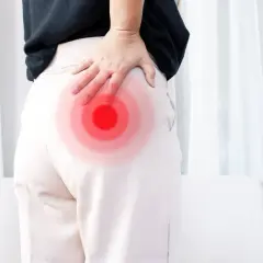 Une femme se tient le fessier droit, marqué par des cercles rouges, suggérant une douleur. La signification de cette douleur fessier droit peut varier.
