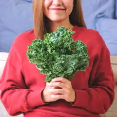 Une femme souriante tient un bouquet de chou kale, un légume aux multiples chou kale bienfaits pour la santé.