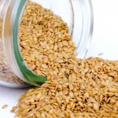 Graines de lin dorées renversées d'un bocal en verre, révélant leurs nombreux bienfaits pour la santé.