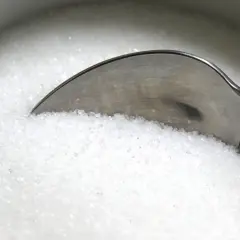 Une cuillère dans un bol de sucre blanc, rappelant les dangers du cholestérol, du sucre ou du sel pour la santé.