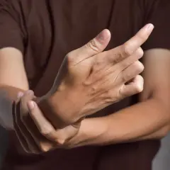 Main tenant une main, l'autre main se tient le poignet, suggérant des symptômes de fonte musculaire.