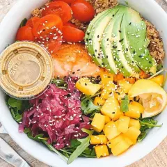 Un bol coloré avec saumon, avocat, tomates, mangue et chou rouge. Une assiette saine pour savoir comment faire baisser son taux d'insuline naturellement.