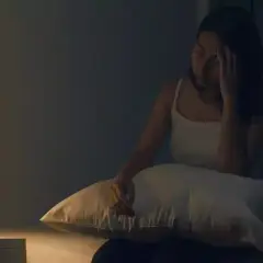 Femme insomniaque, le front serré, envisageant une cure de magnésium. Sur la table de nuit, une lampe, une bouteille d'eau et des médicaments.