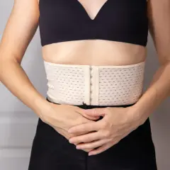 Ceinture de resserrage du bassin, beige, avec fermeture à crochets, portée sous un soutien-gorge noir.