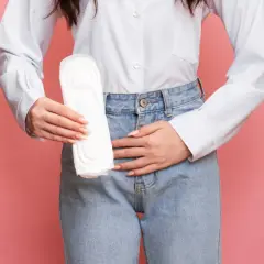 Une femme tient une serviette hygiénique, le ventre douloureux, symbolisant la douleur de règle sans règle.