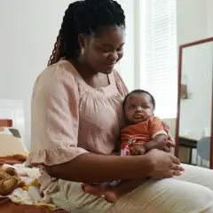 Une mère tient son bébé, un moment tendre malgré les sueurs nocturnes post partum. Un ours en peluche est posé sur le lit.