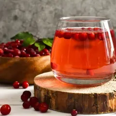 Verre de jus de cranberry, fruit réputé pour aider contre l'infection urinaire. Baies rouges dans un bol en bois.