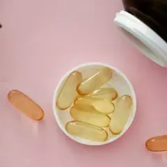 Gélules de collagène et vitamine C sur fond rose, à côté d'une feuille verte.