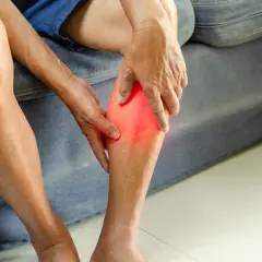 Main tenant sa jambe, une personne ressent une douleur vive, se demandant combien de temps d'arrêt de travail pour une déchirure musculaire.