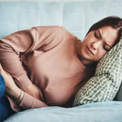 Femme souffrant de SPM, se tenant le ventre sur un canapé. Combien de temps avant que la douleur ne passe ?