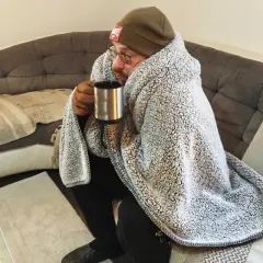 Un homme emmitouflé dans une couverture, tenant une tasse chaude, se demande pourquoi j'ai froid alors qu'il fait chaud.