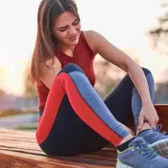 Une coureuse s'assoit sur un banc, se tenant la cheville avec une expression de douleur. La douleur à la cheville après la course à pied peut être débilitante.