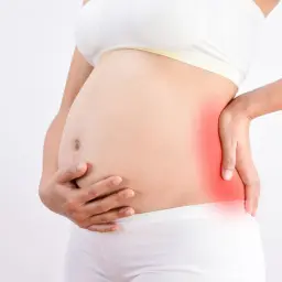 Femme enceinte tenant son ventre, une zone rouge sur le côté indique une douleur au fessier en fin de grossesse.