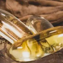 Trois capsules d'oméga 3 dorées reposent sur une noix. Quand prendre oméga 3 pour un bien-être optimal ?