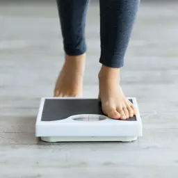 Pieds nus sur une balance, scrutant une possible perte de poids inexpliquée.
