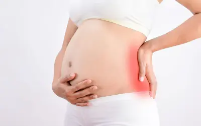 Femme enceinte tenant son ventre, une zone rouge sur le côté indique une douleur au fessier en fin de grossesse.