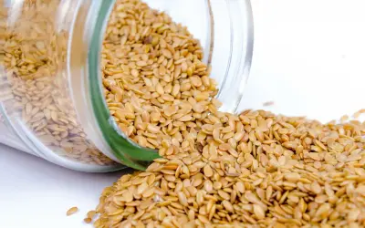Graines de lin dorées renversées d'un bocal en verre, révélant leurs nombreux bienfaits pour la santé.
