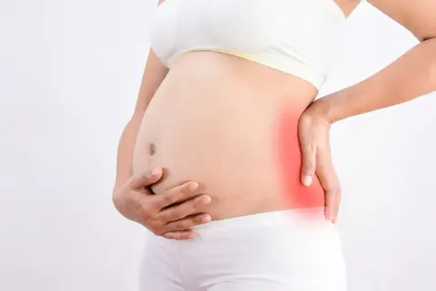 Femme enceinte tenant son ventre, une zone rouge sur le côté indique une douleur au fessier en fin de grossesse.