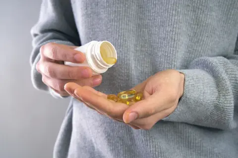Main tenant une capsule d'huile de poisson dans sa main, prêt à prendre son complément. Avis sur les oméga 3.
