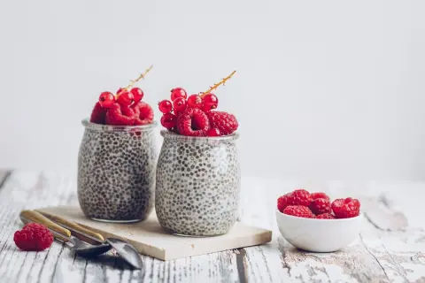 Deux pots de crème de chia garnis de framboises et de groseilles. Un petit bol de framboises à côté. Parfait pour une graine de chia enceinte.