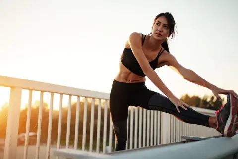 Femme s'étirant les ischio-jambiers, une conséquence d'un entraînement intense. Le soleil se lève sur un paysage flou.
