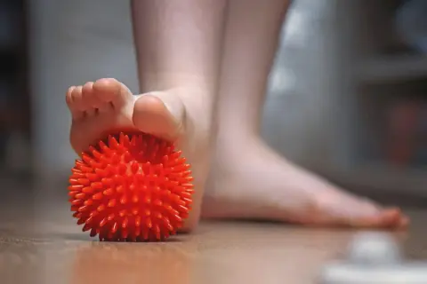 Un pied utilise une balle rouge texturée pour soulager une tendinite sous le pied.