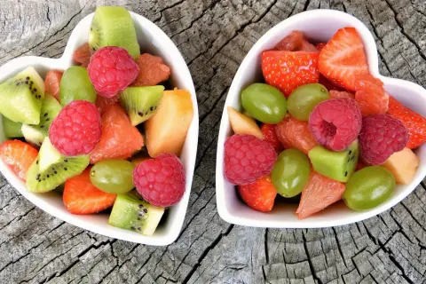 Deux bols en forme de cœur remplis de fruits non acides : fraises, framboises, kiwis, raisins, melon et pamplemousse.