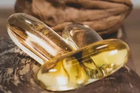 Trois capsules d'oméga 3 dorées reposent sur une noix. Quand prendre oméga 3 pour un bien-être optimal ?