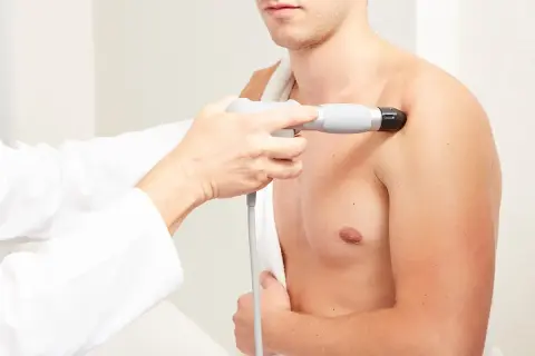 Thérapeute appliquant des ondes de choc radiales sur l'épaule d'un patient pour soulager la douleur.