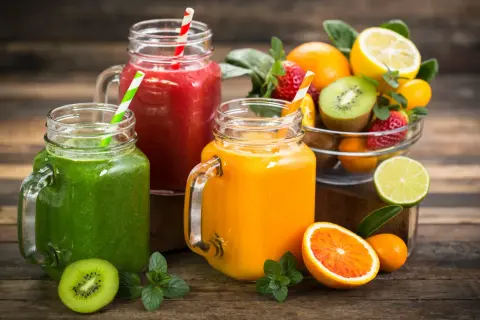Trois smoothies colorés (vert, rouge, orange) dans des bocaux en verre, accompagnés de fruits frais. Parfait pour une cure detox maison.