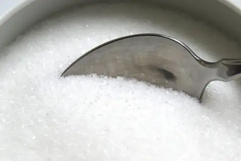 Une cuillère dans un bol de sucre blanc, rappelant les dangers du cholestérol, du sucre ou du sel pour la santé.