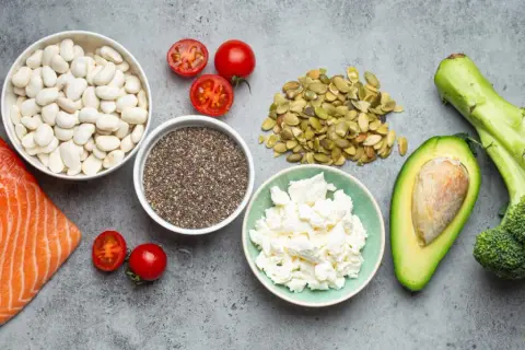 Saumon, haricots blancs, tomates, graines de chia, fromage blanc, avocat et brocoli sur fond gris.