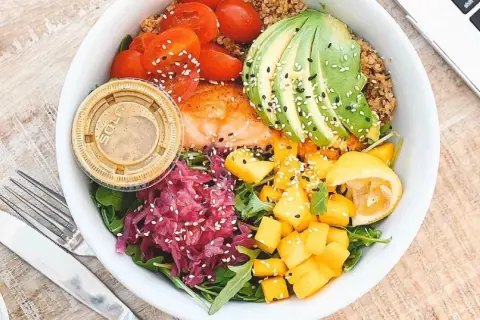 Un bol coloré avec saumon, avocat, tomates, mangue et chou rouge. Une assiette saine pour savoir comment faire baisser son taux d'insuline naturellement.