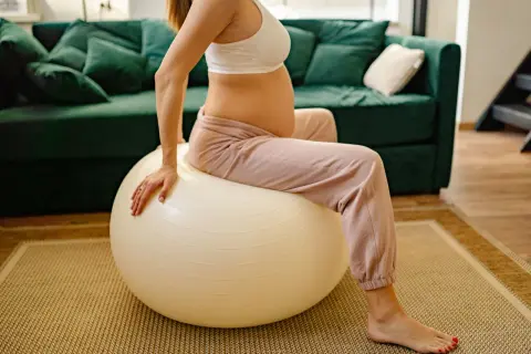 Femme enceinte assise sur un ballon de gym pour un exercice d'ouverture du col.