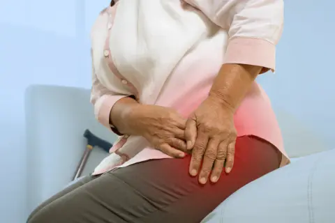 Une personne âgée ressent une douleur à la hanche, peut-être due à une ancienne blessure de course à pied. Une canne est visible à proximité.