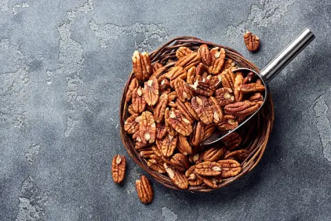 Un panier rempli de noix de pécan, une cuillère métallique en extrait. Savourez les noix de pécan, un concentré de bienfaits pour la santé.